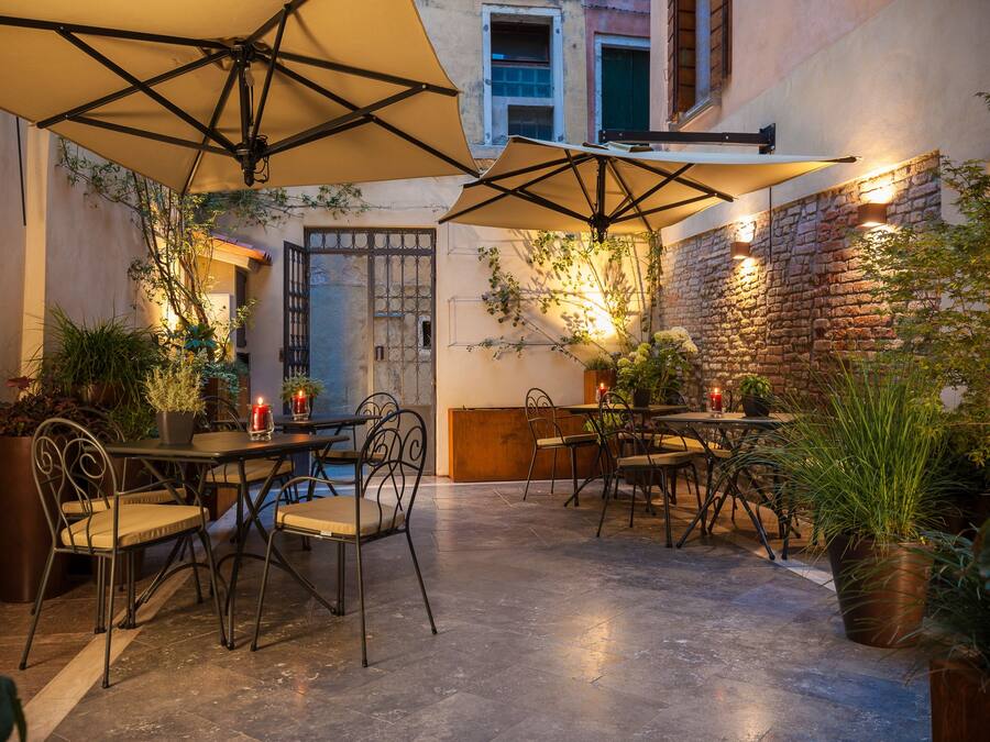 An outdoor café with tables and chairs, surrounded by potted plants and a brick wall.