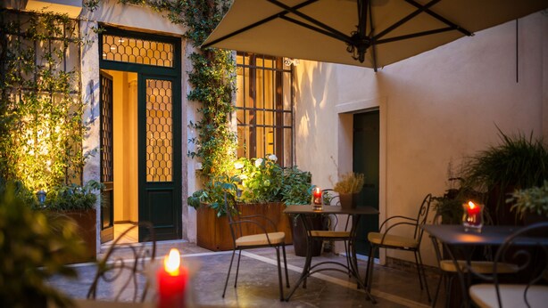 Un patio al aire libre con mesas y sillas, plantas en macetas y una vela encendida.