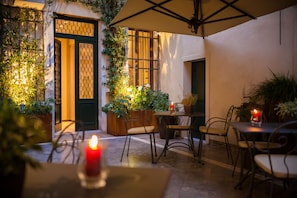 An outdoor patio area with tables and chairs, potted plants, and a lit candle. - Liassidi Wellness Suites (Venice)