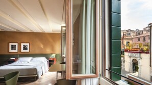 Habitación de hotel con cama, escritorio, silla y un amplio ventanal con vista a edificios.