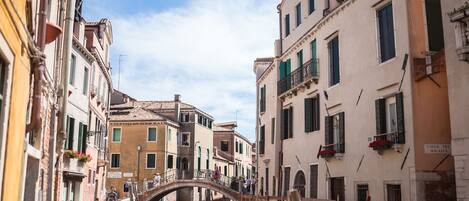 A narrow canal in a historic European town with buildings on either side, a bridge, and a sign for 'Calle del Magazio'.