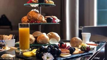 A breakfast buffet with various pastries, fruits, and a glass of orange juice on a marble countertop.