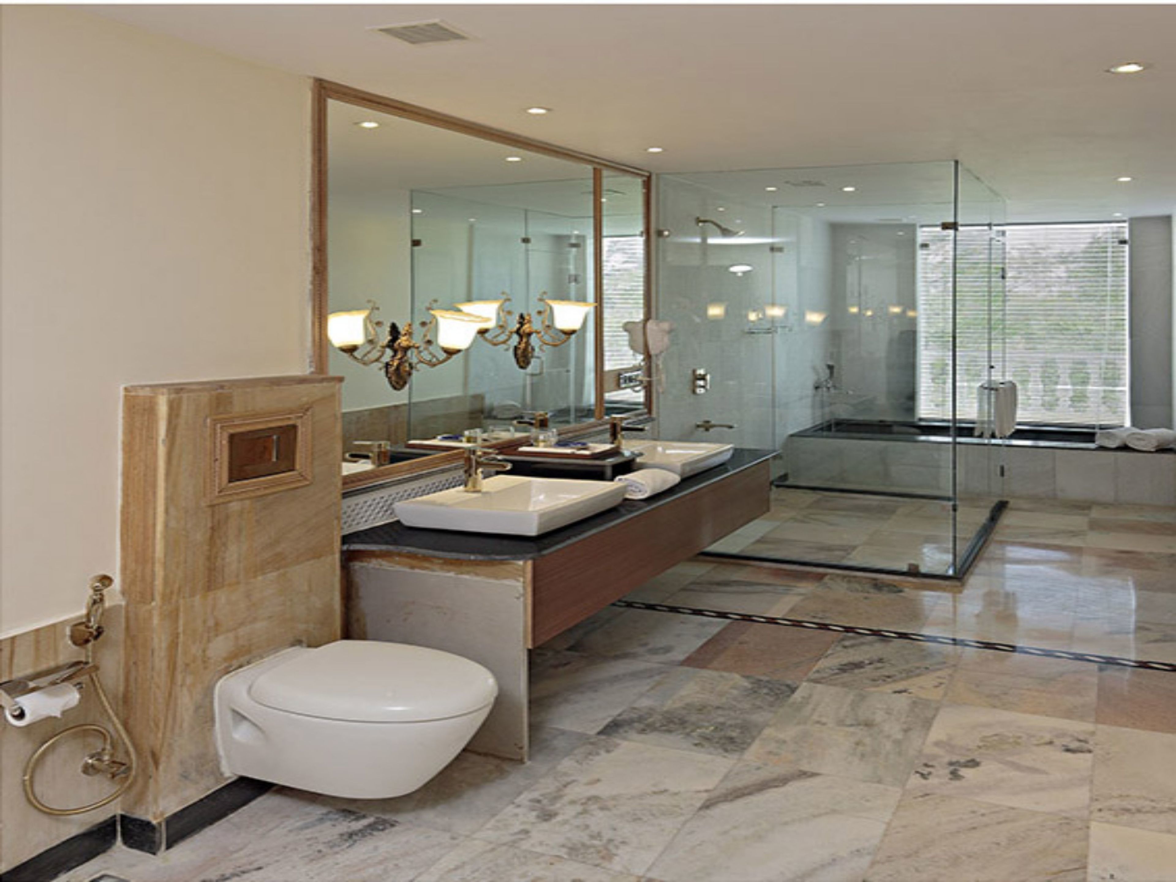 A modern bathroom with a large mirror, two sinks, a toilet, and a glass-enclosed shower area.
