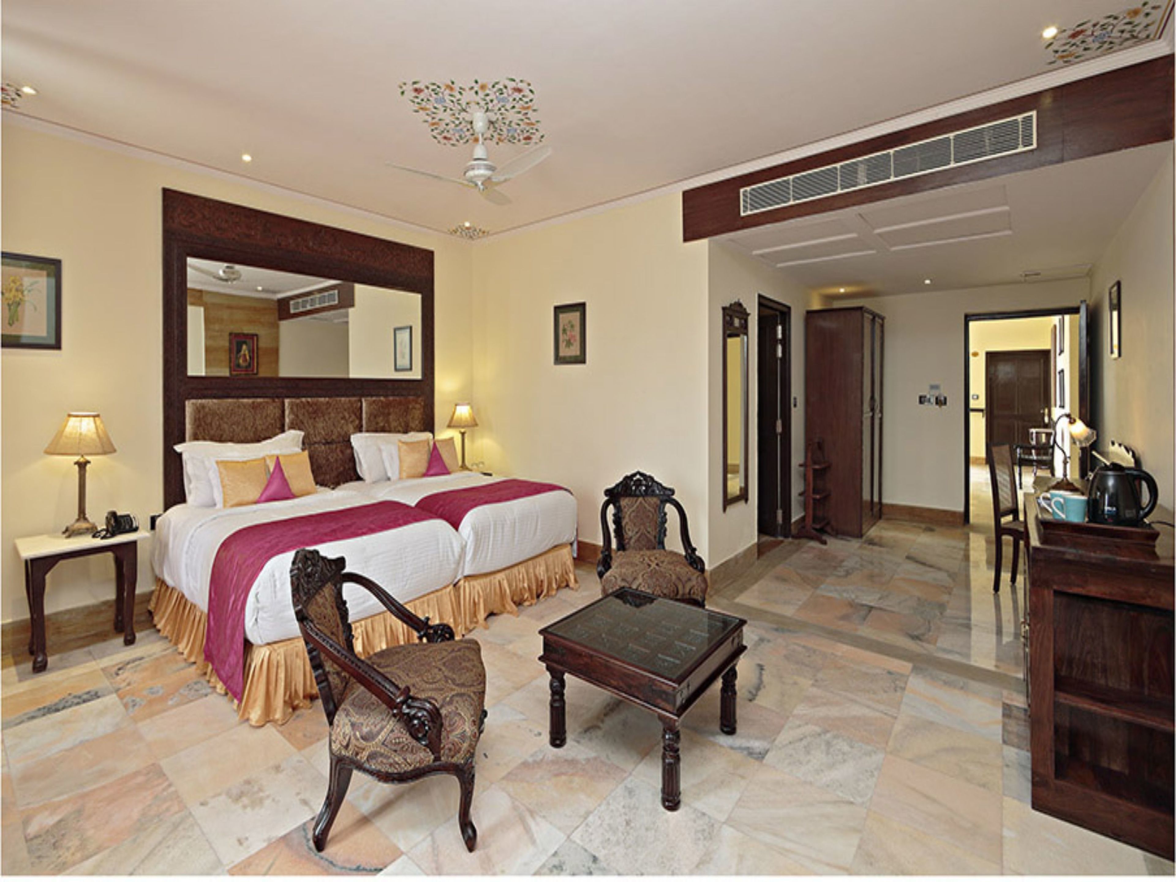 Une chambre d’hôtel avec un grand lit, deux chaises, une table et un ventilateur de plafond.