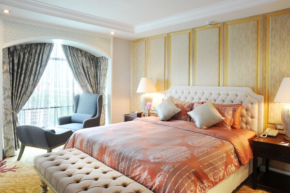 A spacious bedroom with a large bed, a chair, and a desk with a lamp.