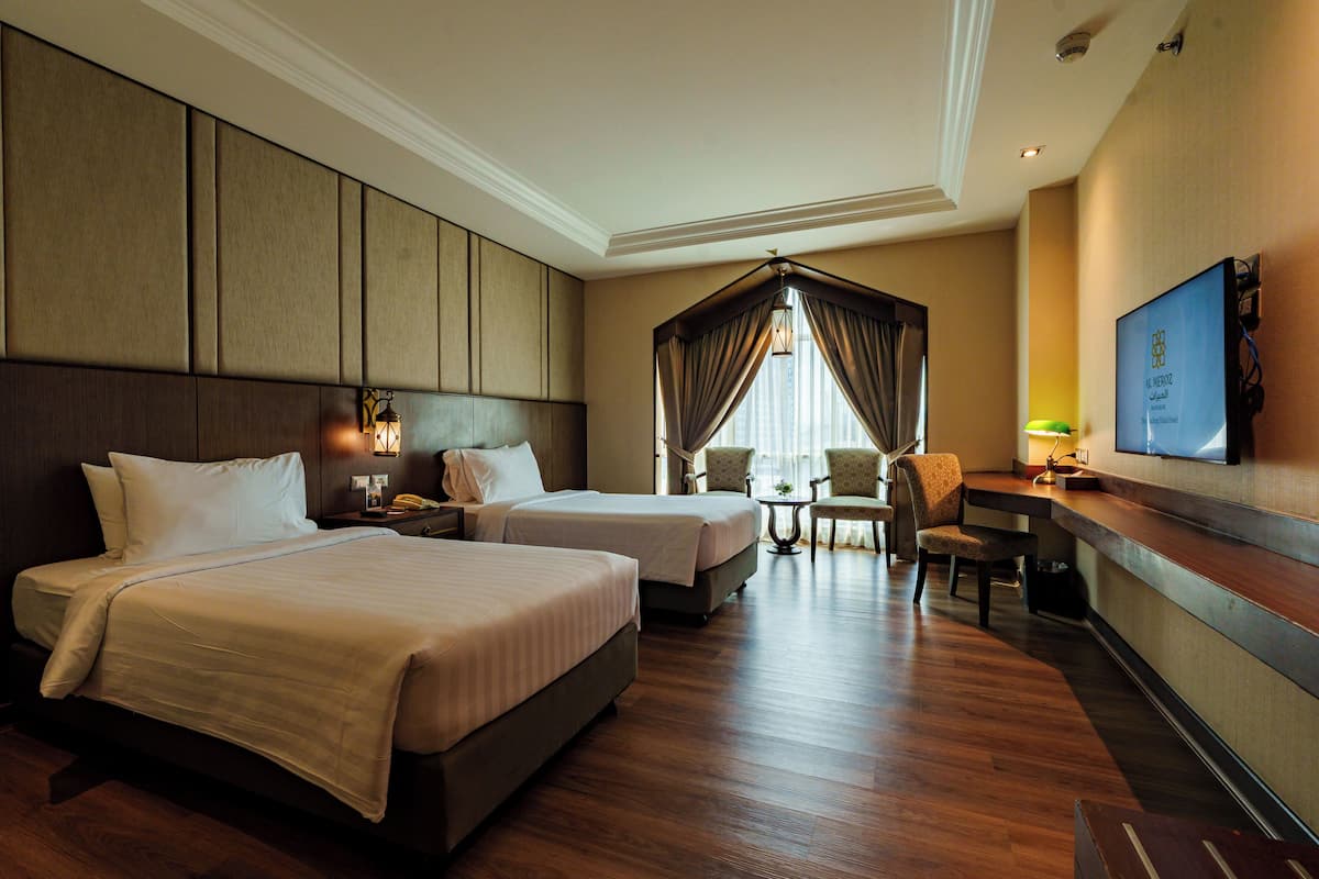 A hotel room with two beds, a desk, a chair, a television, and a window with curtains.