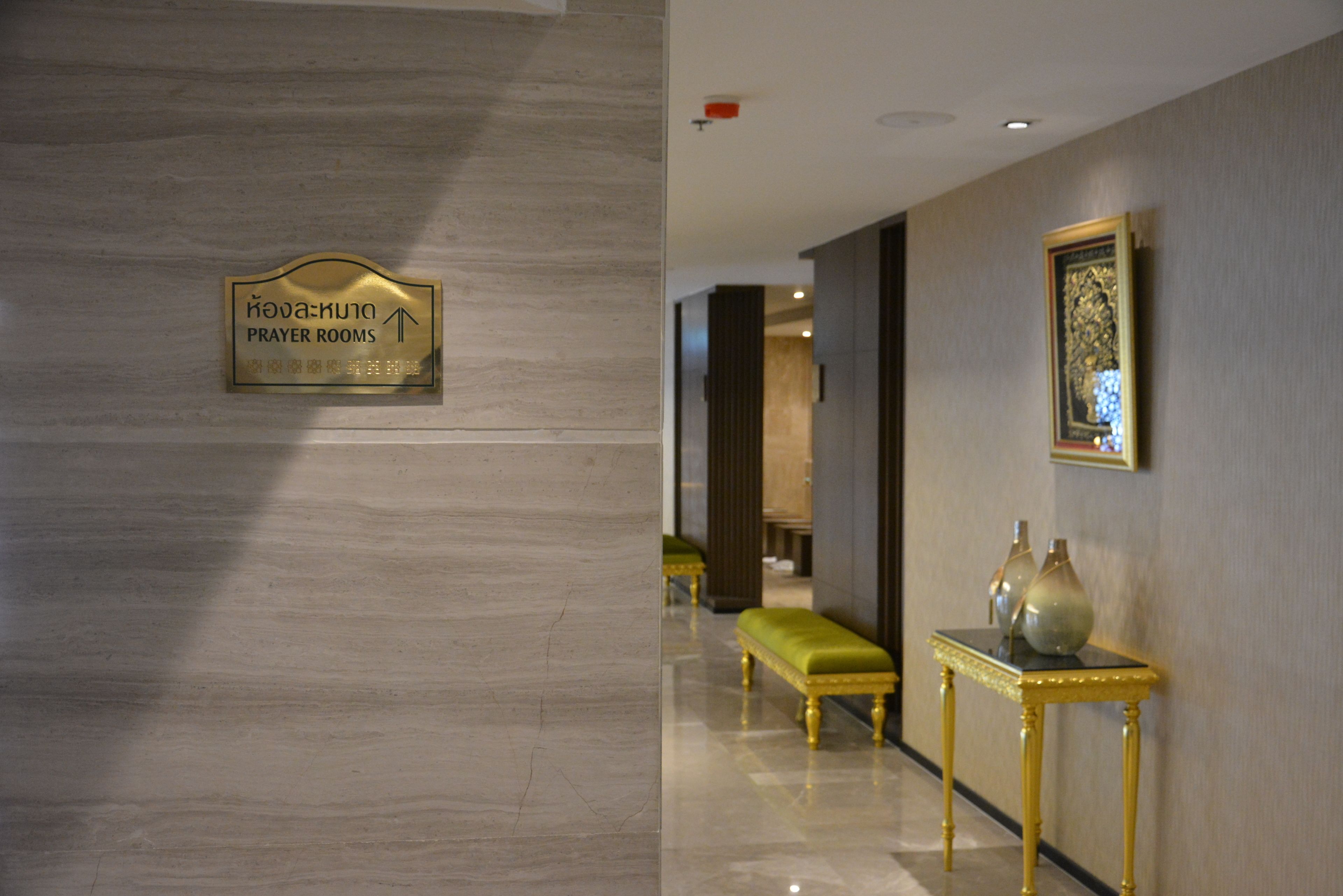 A hallway with a sign indicating prayer rooms, a bench, and a table with vases.
