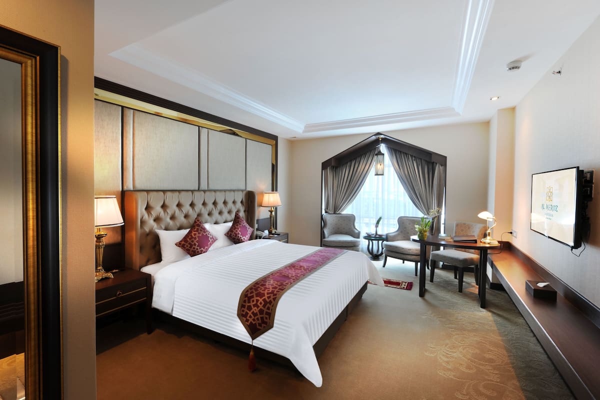 A hotel room with a large bed, a desk, a chair, a TV, and a window with curtains.