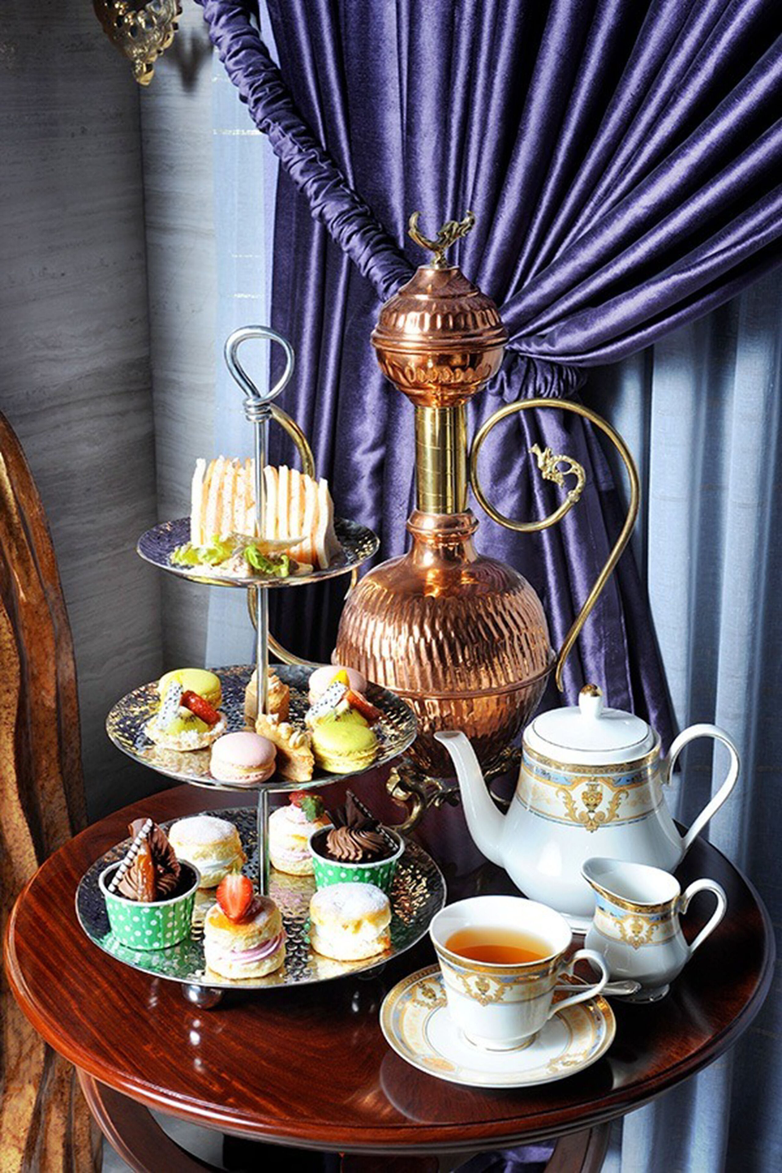 Un présentoir à trois niveaux, garni de diverses pâtisseries, et une théière, le tout posé sur une table.