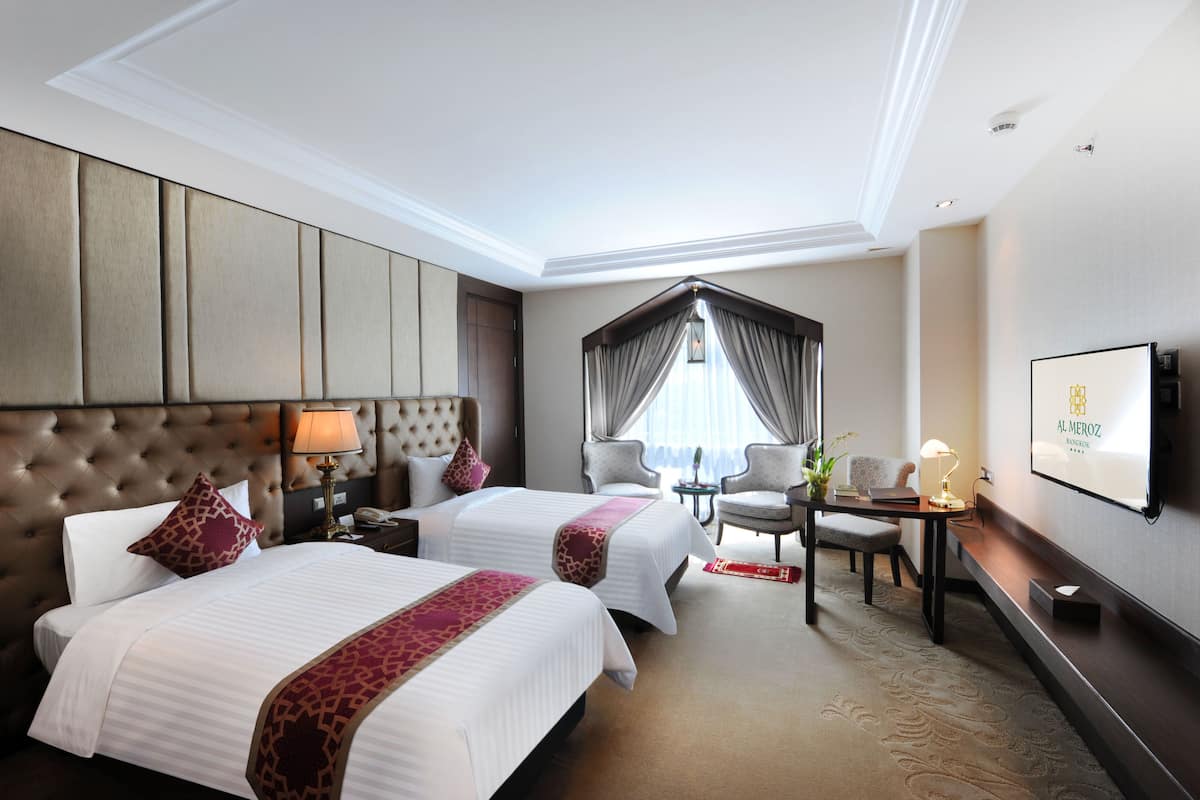 A hotel room with two beds, a desk, a chair, a TV, and a window with curtains.