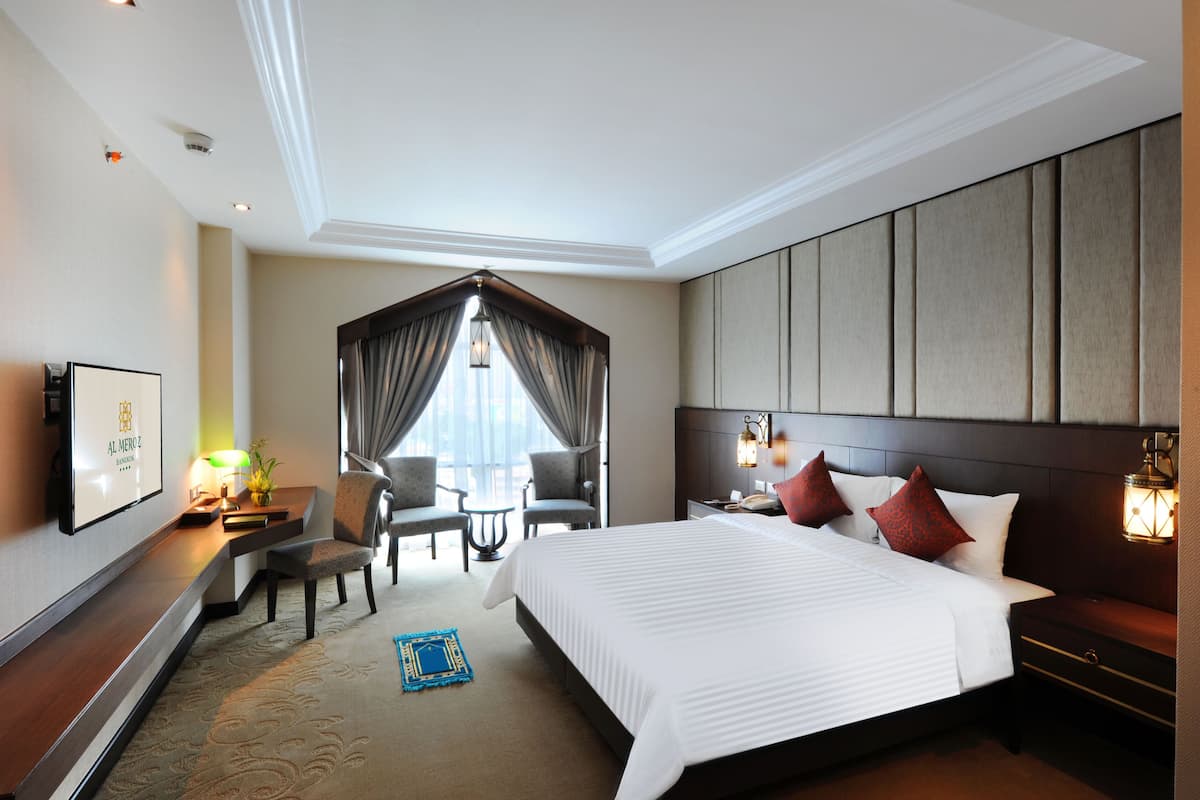 A hotel room with a large bed, a desk with a lamp, two chairs, a TV, and a view of the outdoors.