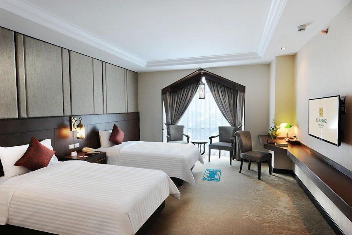 A hotel room with two beds, a desk, a chair, a TV, and a window with curtains.