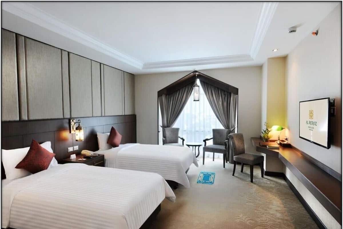 A hotel room with two beds, a sitting area with chairs, a TV, and a large window with curtains.