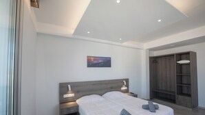 A modern bedroom with a large bed, bedside lamps, a painting on the wall, and a wooden wardrobe. - Pavlinia Hotel Apartments (Ayia Napa)