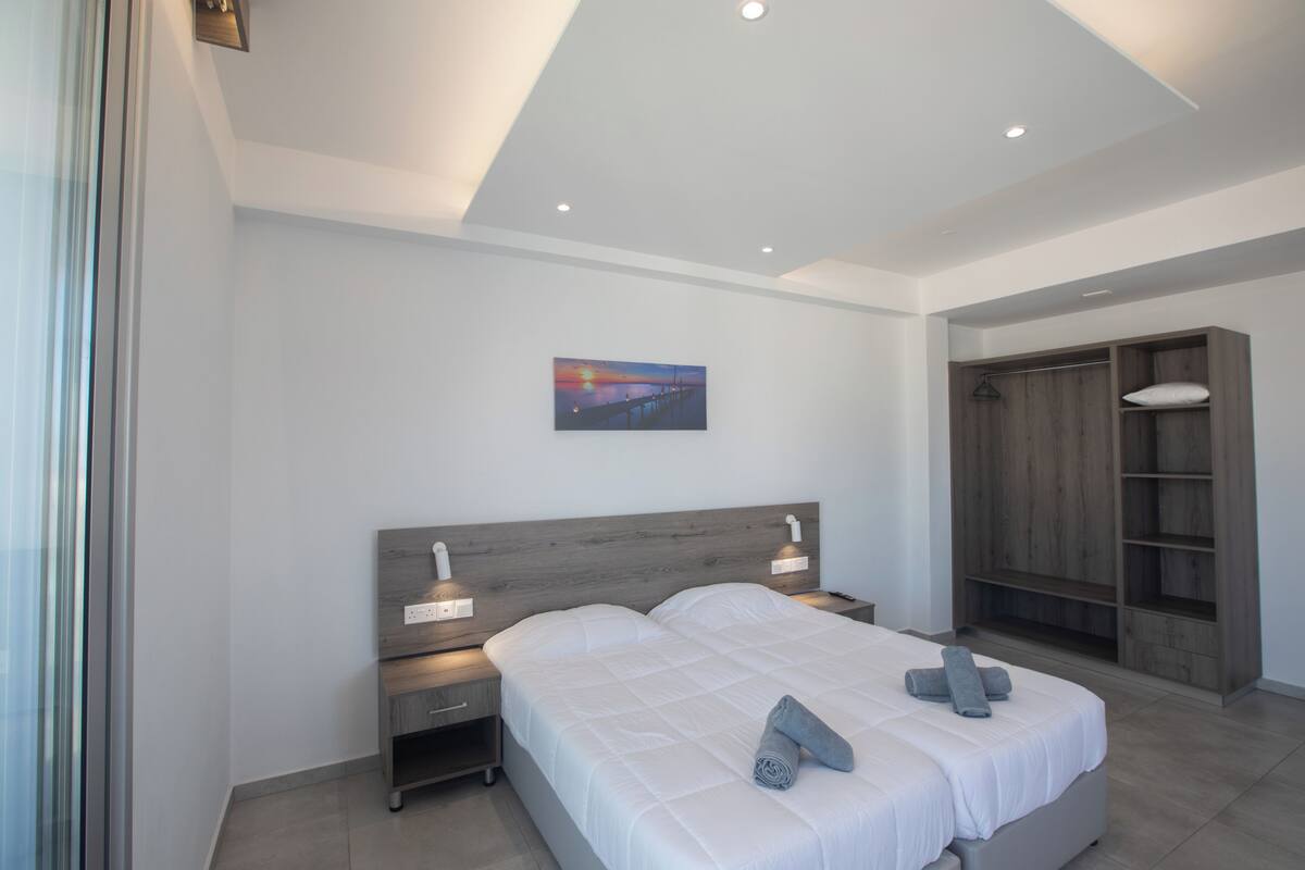 A modern bedroom with a large bed, bedside lamps, a painting on the wall, and a wooden wardrobe.