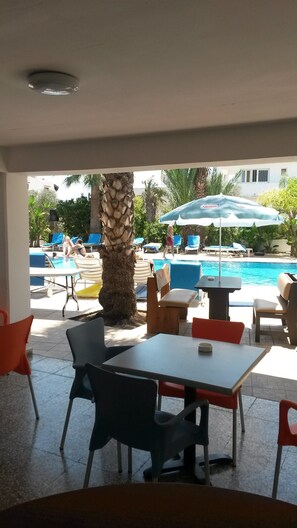 An outdoor seating area with tables and chairs, a pool with lounge chairs, and umbrellas. - Pavlinia Hotel Apartments (Ayia Napa)