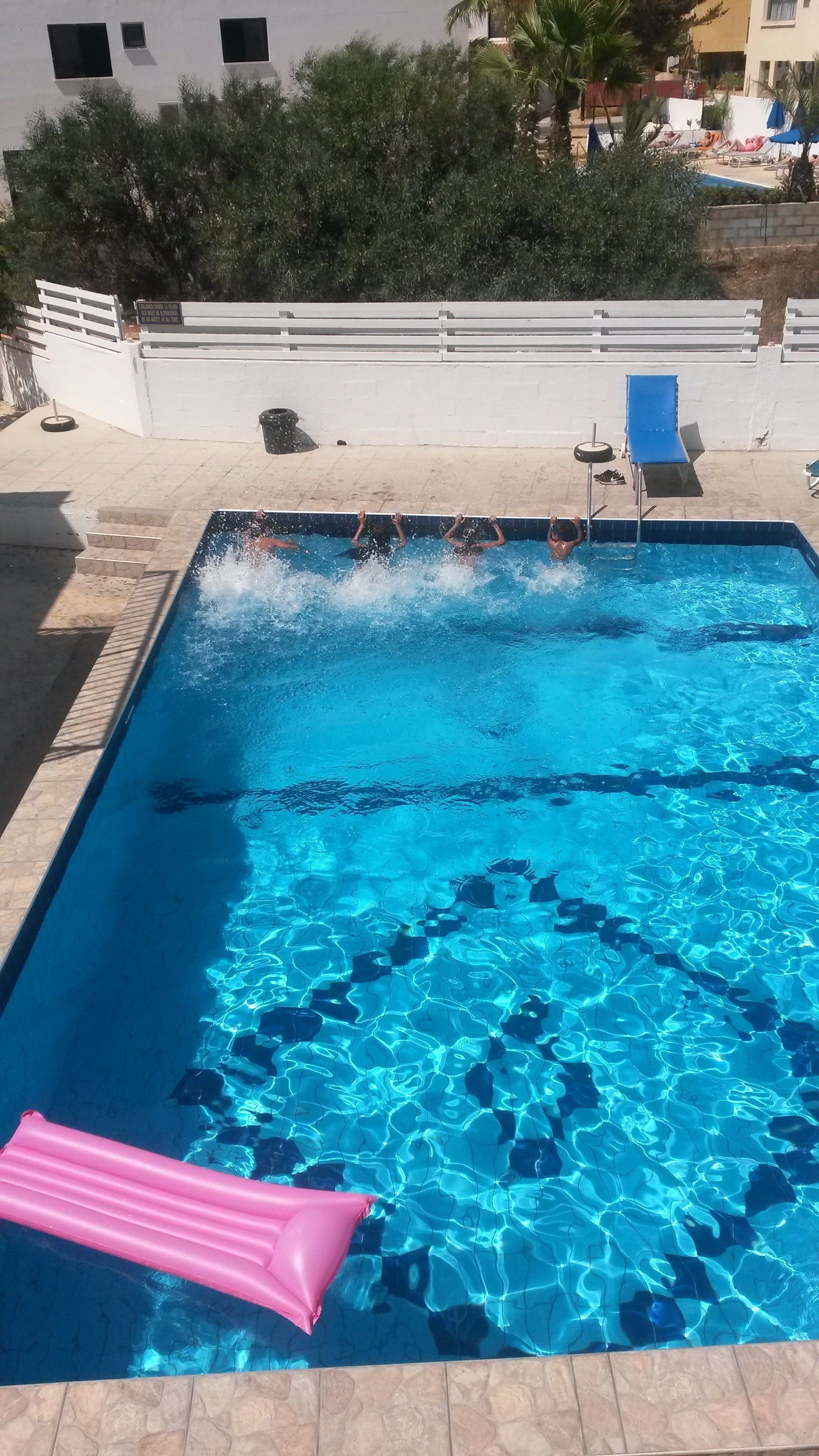 En rektangulær swimmingpool med krystalklart, blåt vand, omgivet af en flisbelagt terrasse.