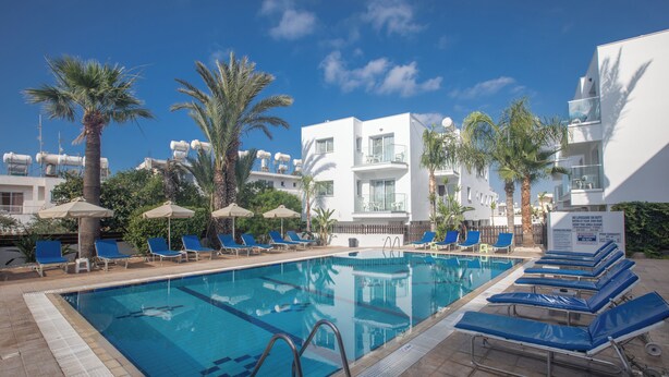A swimming pool with blue lounge chairs and palm trees. - Pavlinia Hotel Apartments (Ayia Napa)
