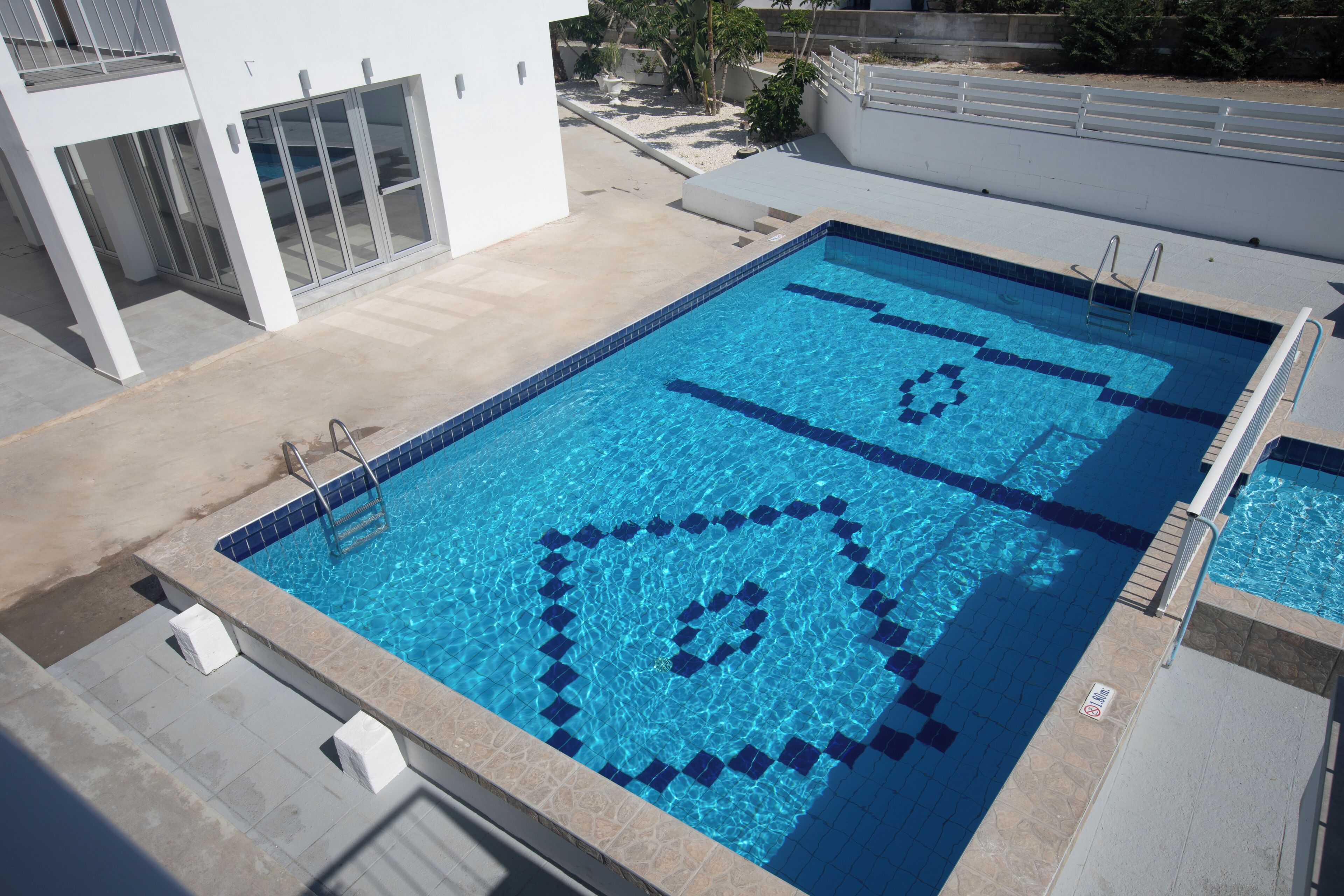 Una piscina rectangular con agua azul cristalina, con un diseño geométrico de azulejos.