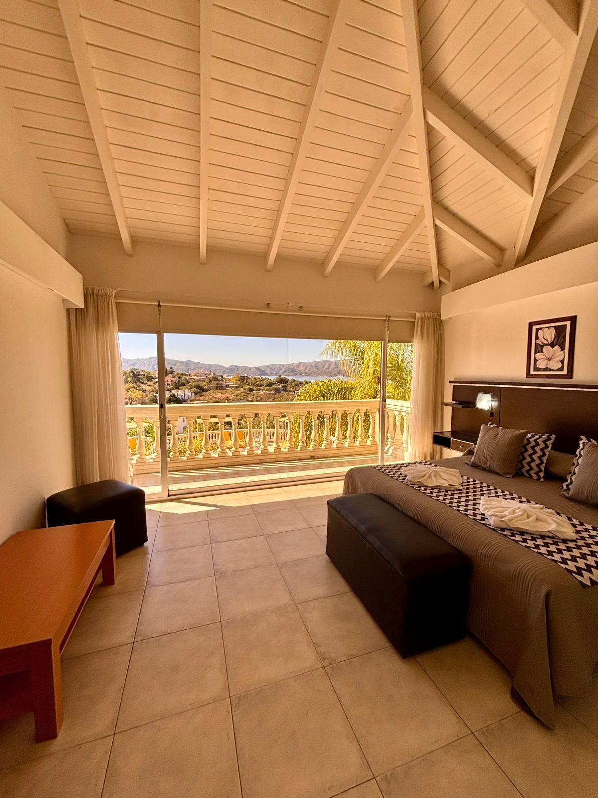 Quarto com cama grande, sofá, mesa pequena e varanda com vista para montanhas.