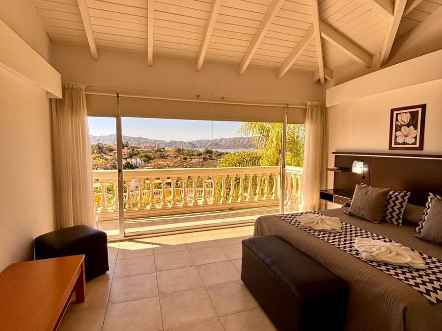 Quarto com cama grande, sofá, mesa pequena e varanda com vista para montanhas.