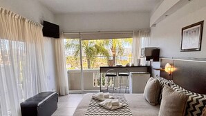 Ein Hotelzimmer mit Bett, Schreibtisch, Stuhl und Blick auf Palmen.