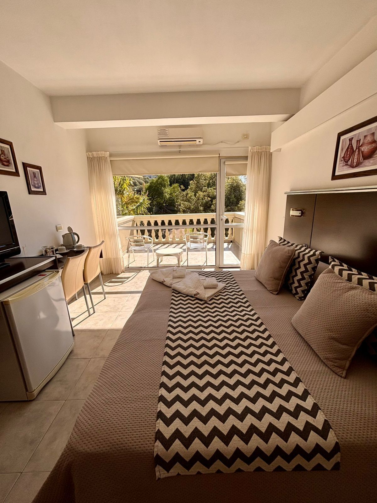 A modern hotel room with a balcony, a sofa, a TV, and a dining area.