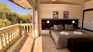 Ein Schlafzimmer mit Balkon, einem Bett mit kariertem Überwurf, einem Kopfteil und zwei gerahmten Bildern an der Wand.