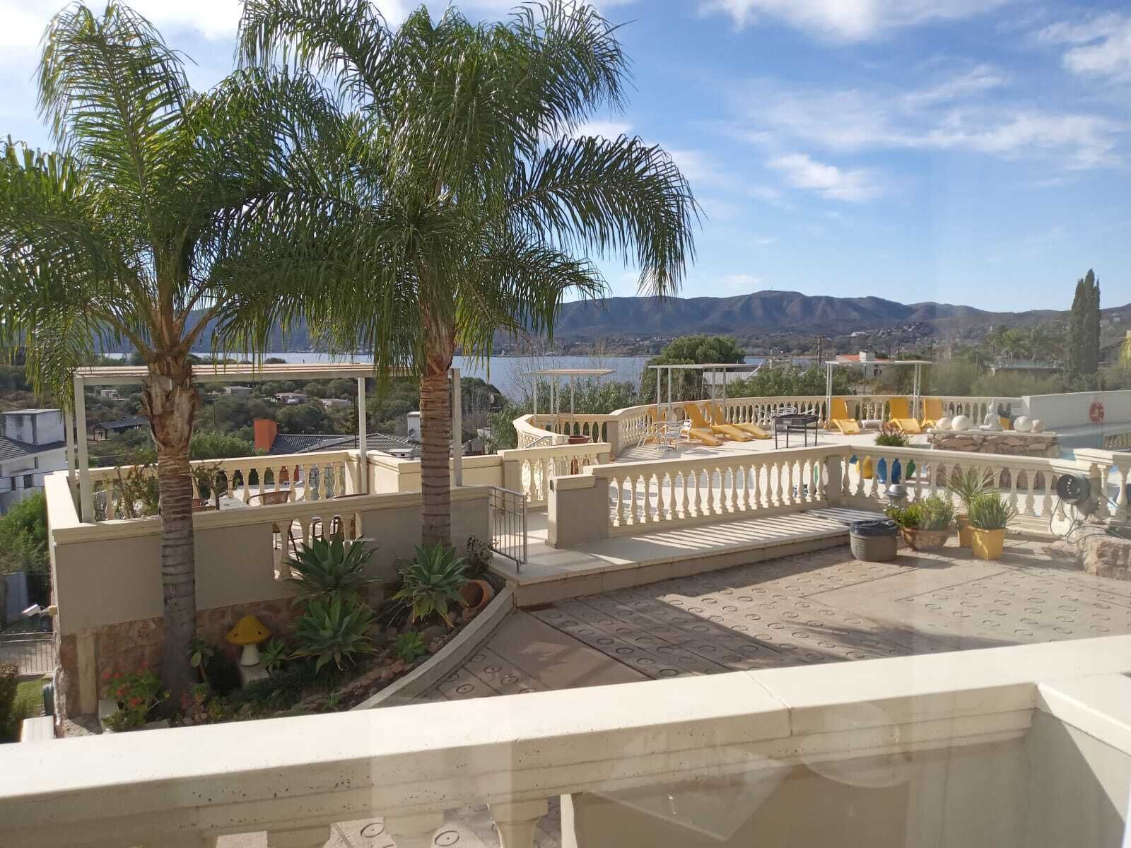 A rooftop terrace with palm trees, a pool, and a view of the mountains.