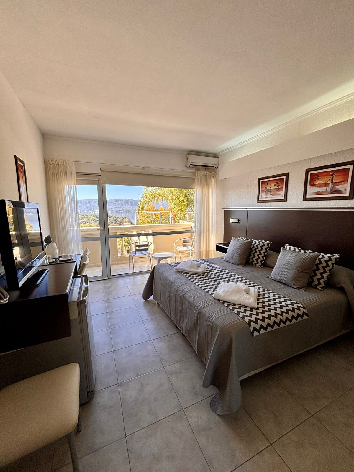 Habitación de hotel con cama, escritorio, silla y balcón con vistas.