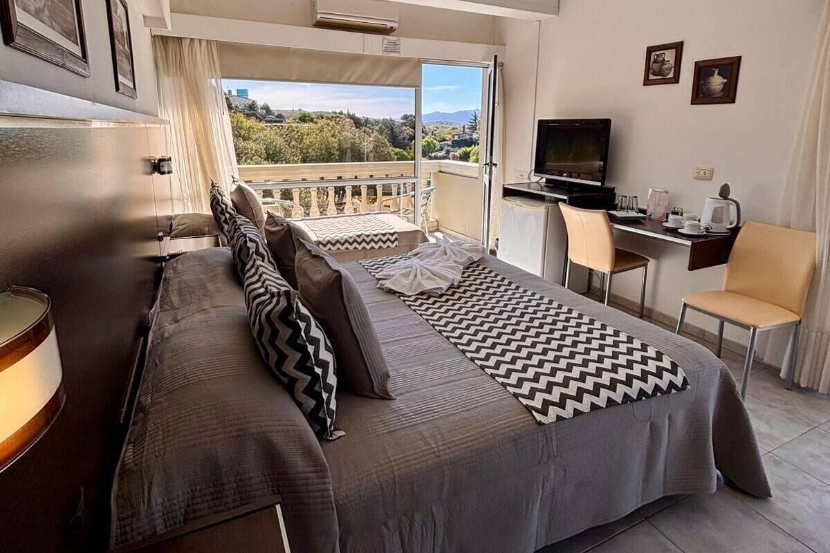 Een hotelkamer met een bed, een bureau, een televisie en een balkon met uitzicht.