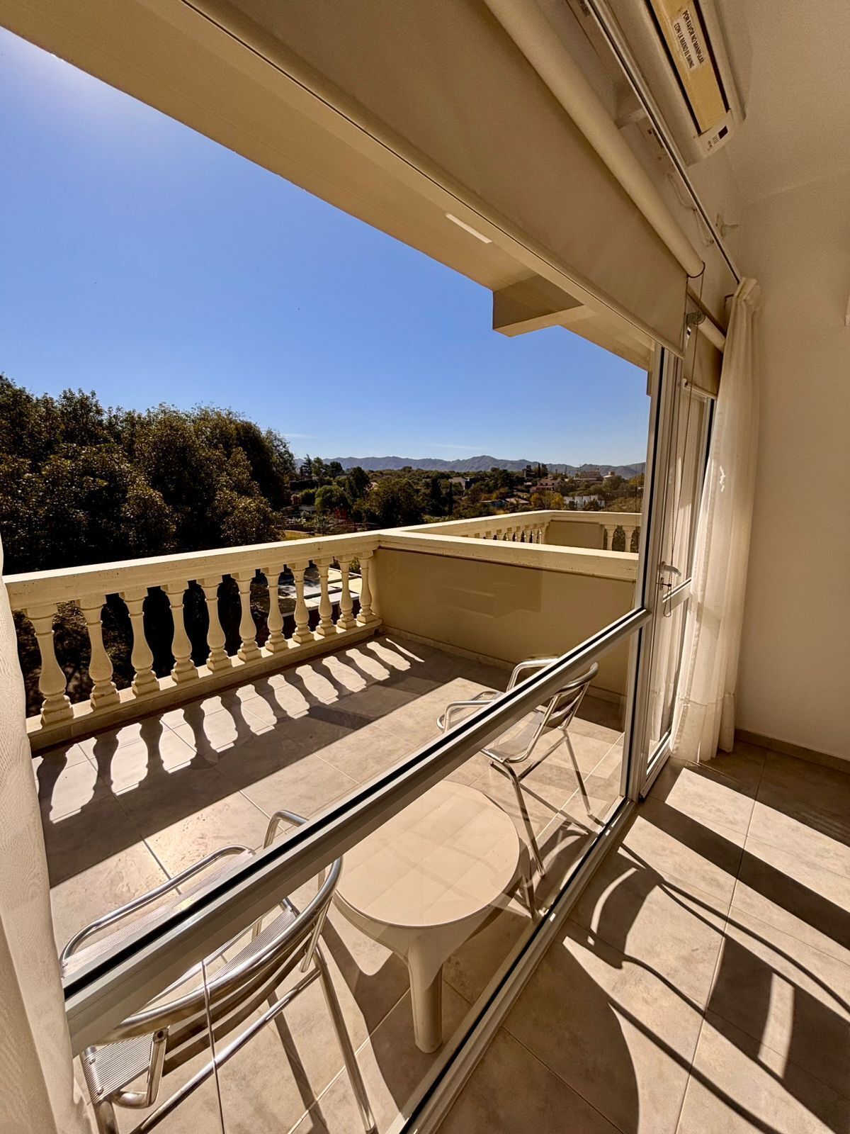 A balcony with a table and chairs, a railing, and a view of the landscape.