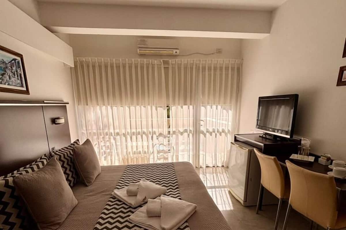 Een hotelkamer met een bed, een bureau met een computer, een televisie en een raam met gordijnen.