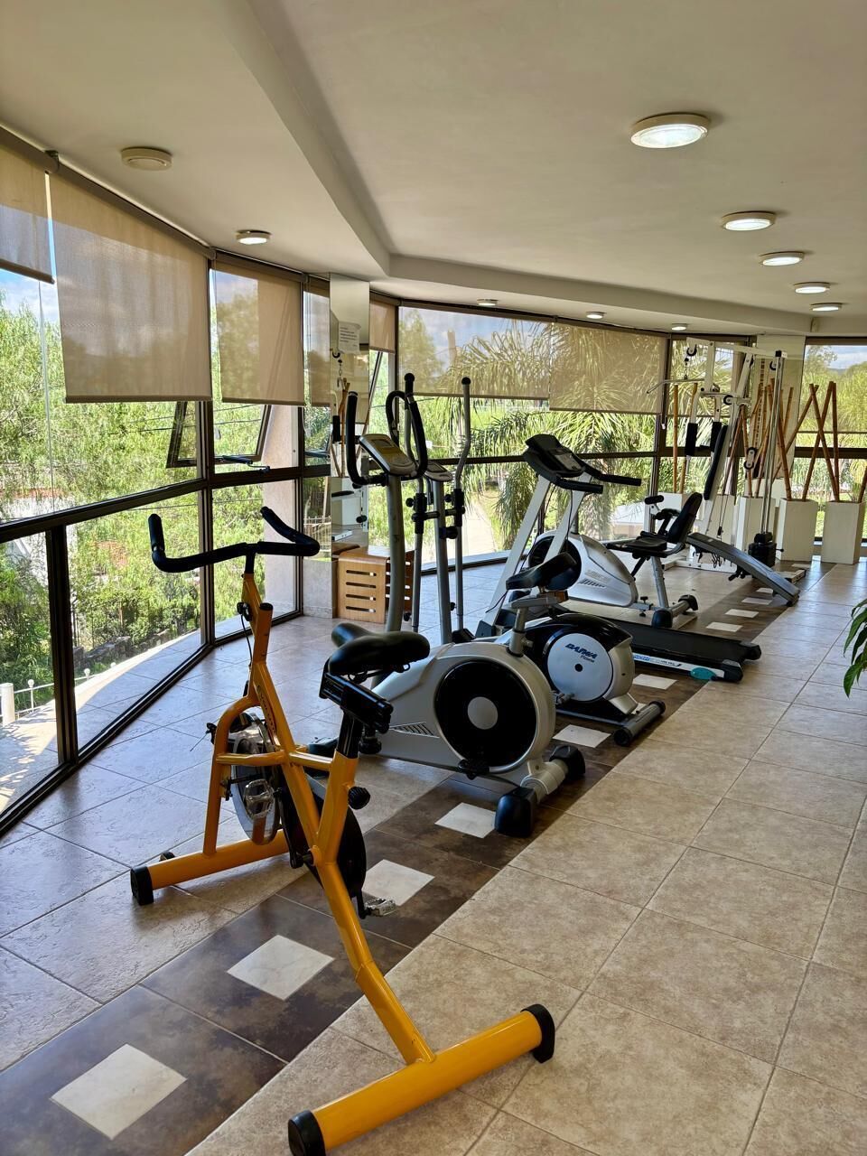 A gym with exercise equipment, large windows, and a tiled floor.