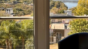 Ein Zimmer mit einem großen Fenster mit Blick auf einen See und Hügel, ein schwarzer Ledersessel und eine Aussicht auf die umliegende Landschaft.