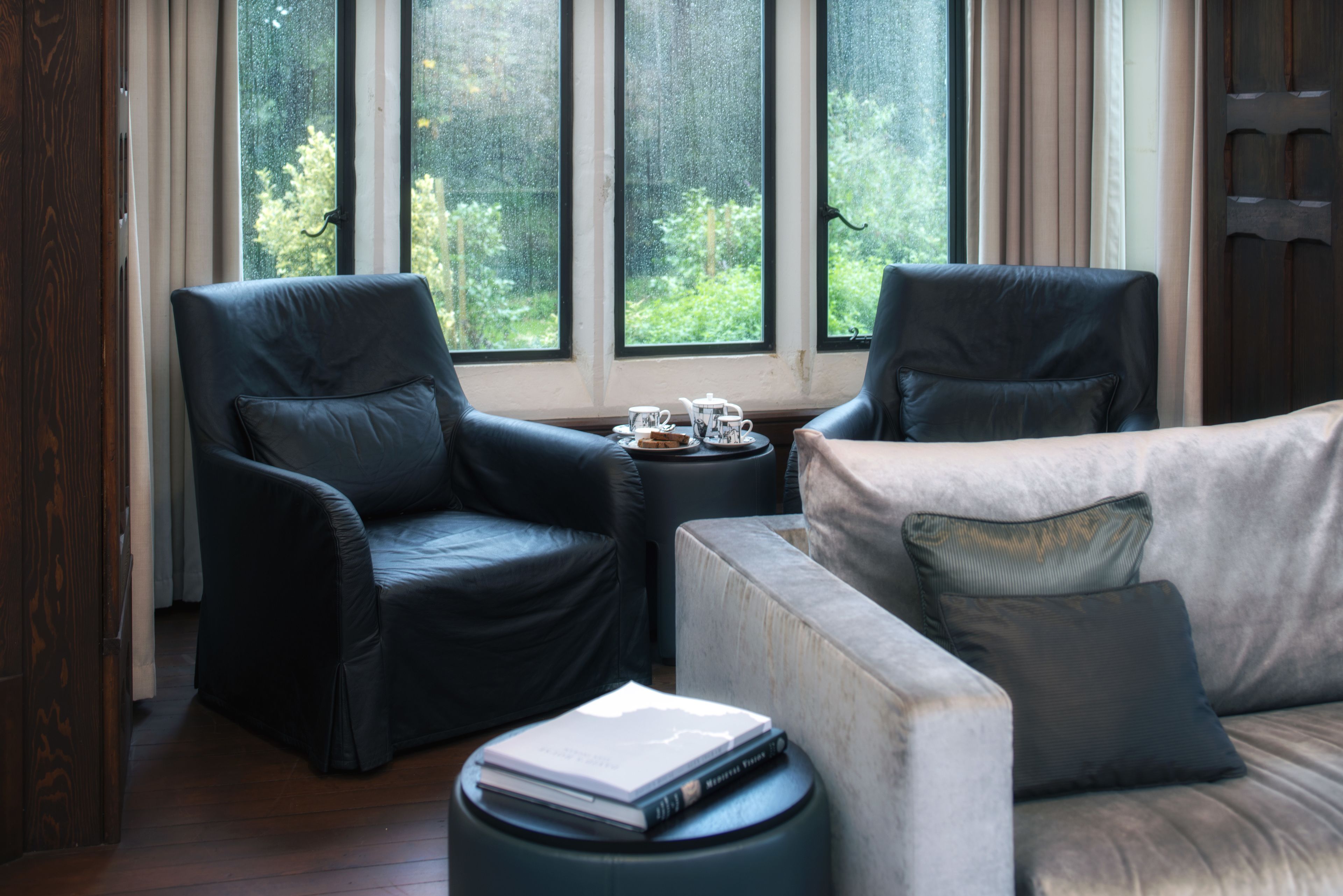A modern living room with two black leather armchairs, a grey sofa, and a small round table with a teapot and cups.