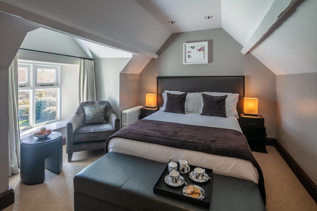 A modern bedroom with a large bed, a chair, a small table with a tray of breakfast, and a window with curtains.