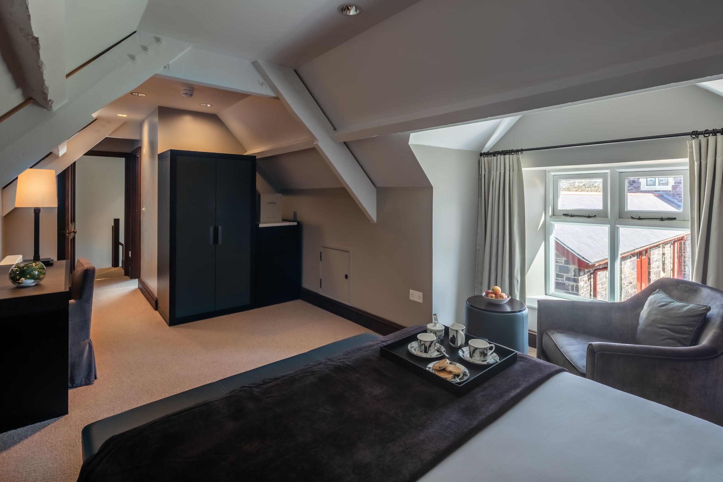 Habitació d'hotel moderna amb sostre alçat, un llit gran, zona de seients amb un safata de petit esmorzar i vista exterior.