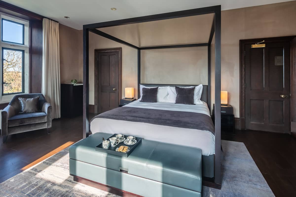 A four-poster bed with a tray of breakfast items, a plush sofa, and a large window with curtains.