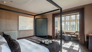Un dormitorio moderno con una cama grande, un armario, una zona de estar con una mesa y vistas a árboles a través de una ventana.