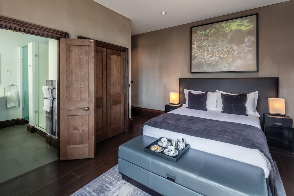 A hotel room with a large bed, a wooden wardrobe, a glass shower, and a framed abstract painting on the wall.