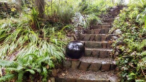 Una escalera de piedra rodeada de exuberante vegetación y un gran jarrón negro.
