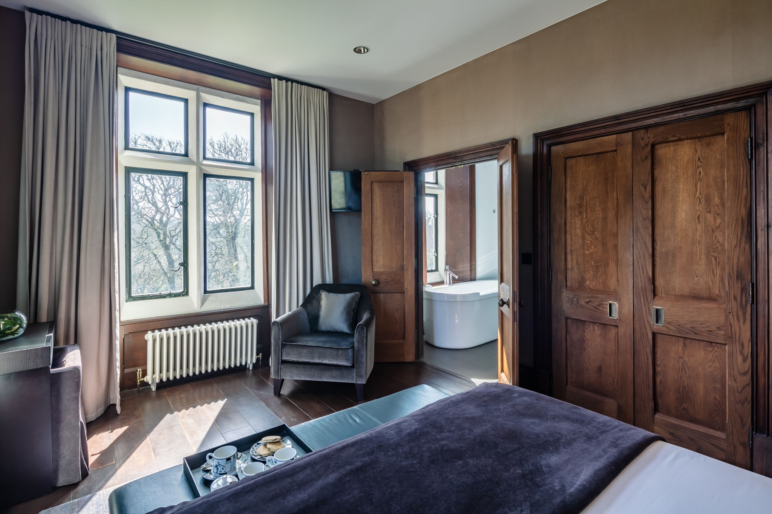 A room with a bed, a chair, a radiator, a window with curtains, and a wooden wardrobe.
