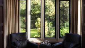 Una habitación con dos sillones de cuero orientados hacia una ventana grande que da a un jardín exuberante.