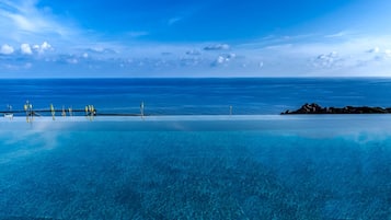 Een buitenzwembad, een infinitypool en ligstoelen