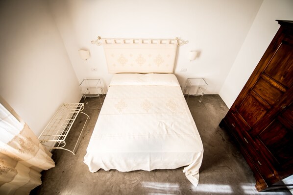 A bedroom with a bed, bedside tables, a wooden wardrobe, and a metal shelf unit.