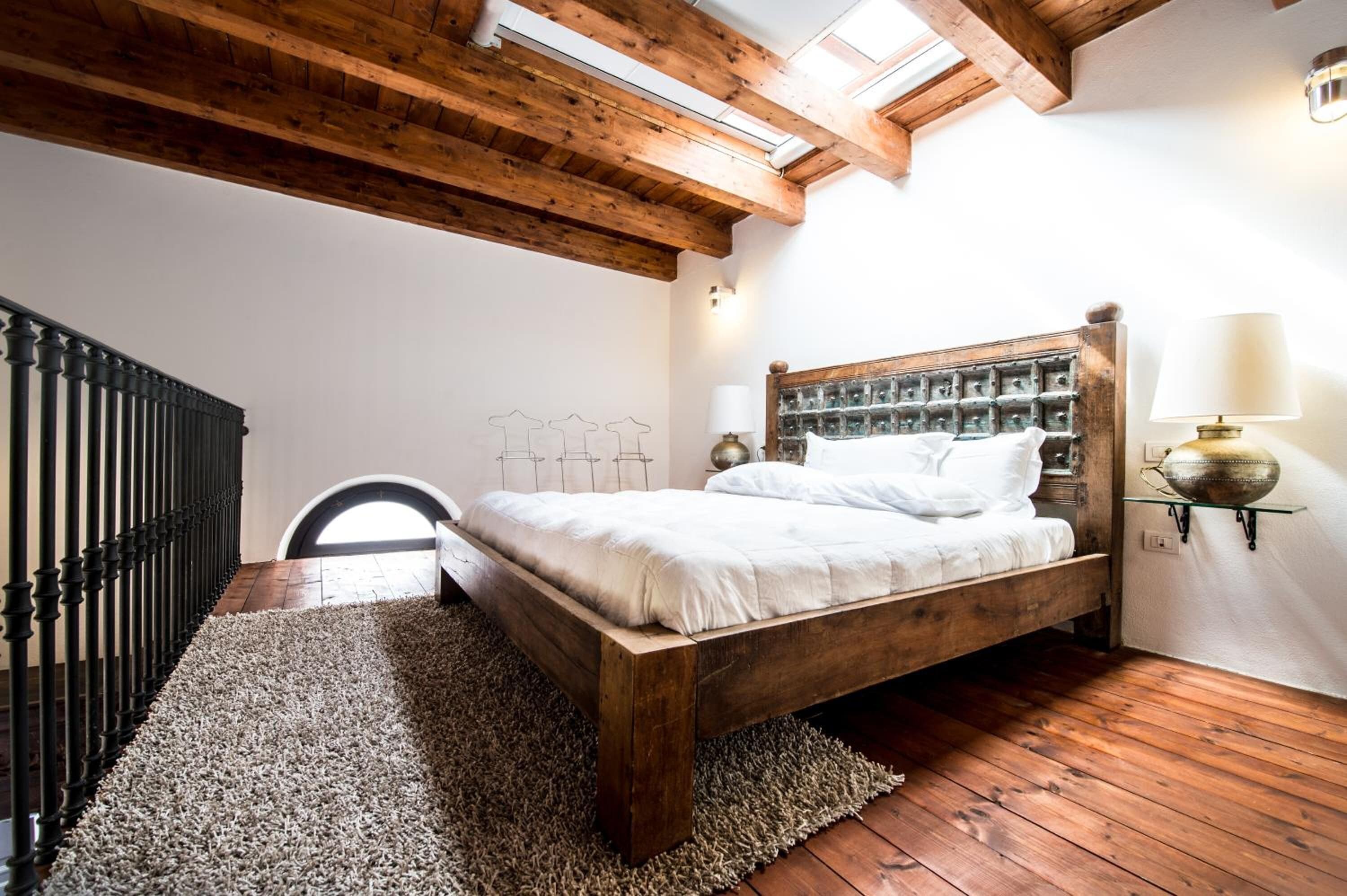 Un dormitorio con cama de madera, baranda negra, tragaluz y vistas al exterior.
