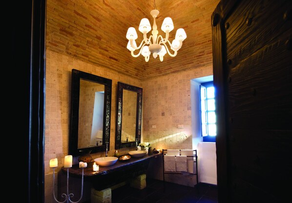 Un baño con techo de madera, un candelabro, dos espejos, un lavamanos, velas y un perchero para toallas.