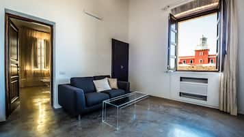 A modern living room with a dark sofa, a glass coffee table, and a view of a red building through a window.
