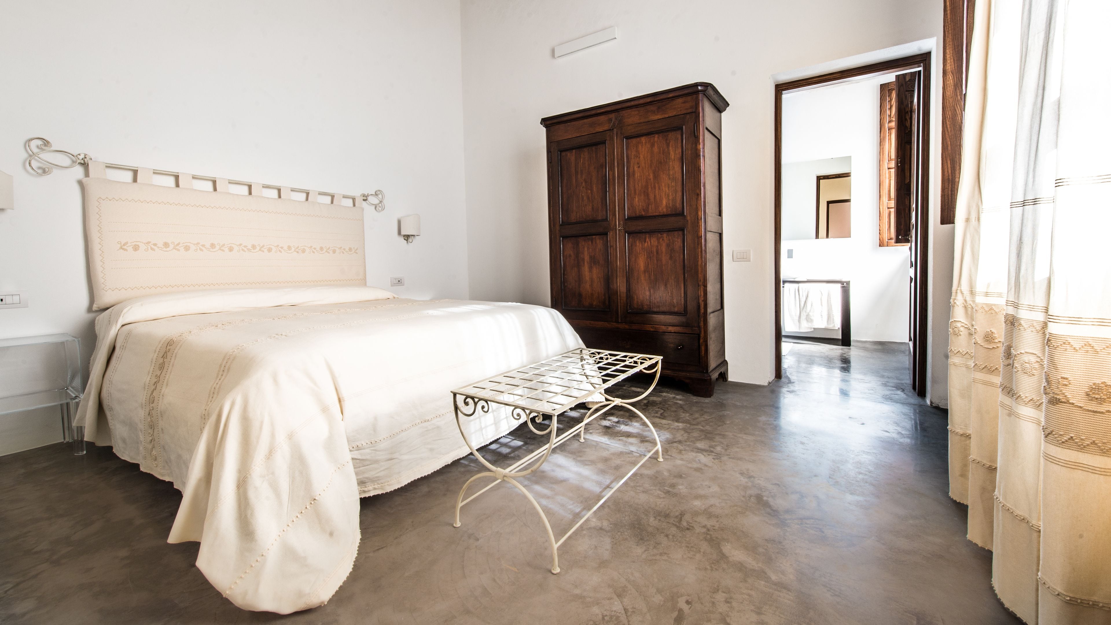 Una camera da letto con un letto, un armadio in legno, una panca in metallo e vista su un corridoio.
